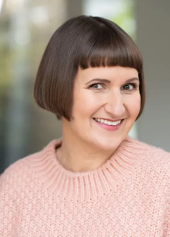 Stephanie Cannon smiling in a pink cardigan with her head tilted to the left